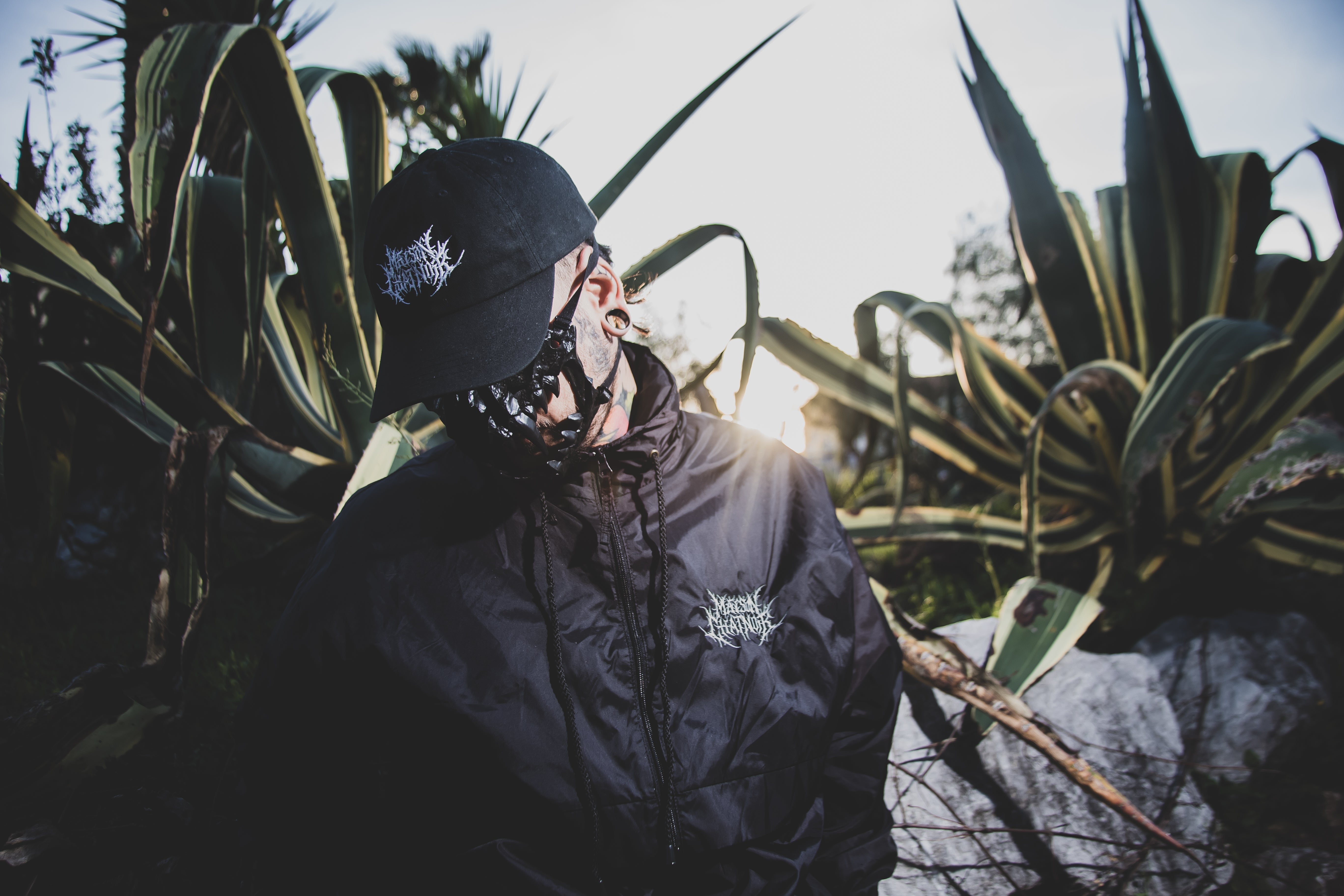 Mannequin portant une casquette et une parka au logo Maison ChatNoir blanc, Masque de chat sur le visage, couché de soleil et cactus