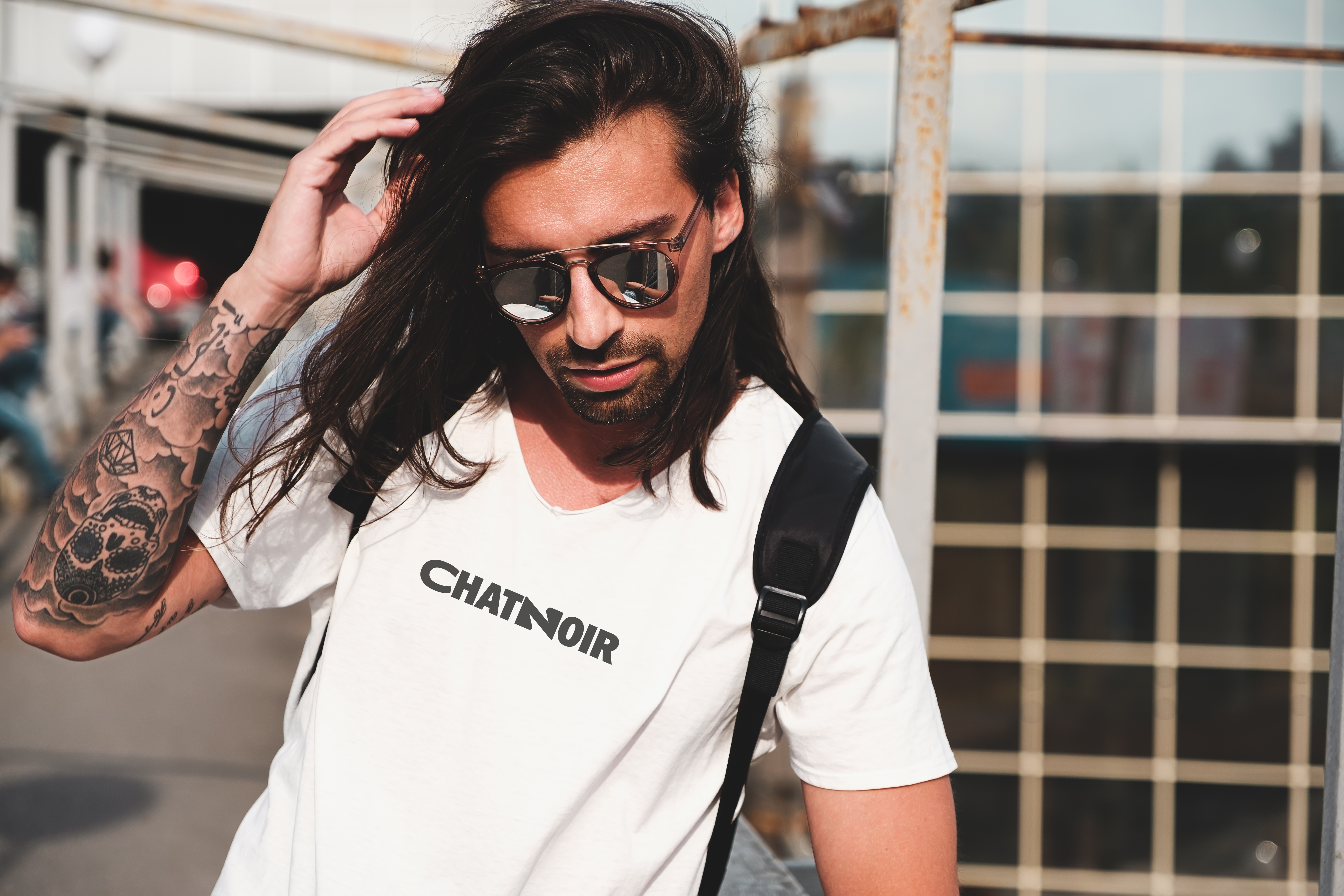 Homme barbu avec lunettes de soleil, t-shirt Chatnoir blanc, tatouage bras, look urbain