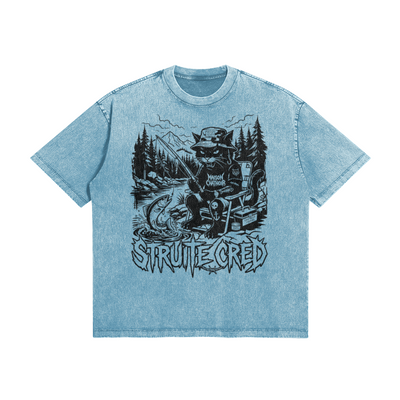 T-shirt bleu avec effet Snow Wash Maison Chatnoir. Graphisme central "StruiteCred" illustrant un chat noir pêcheur de truite dans un style illustration métal, sur un t-shirt à coupe oversized.